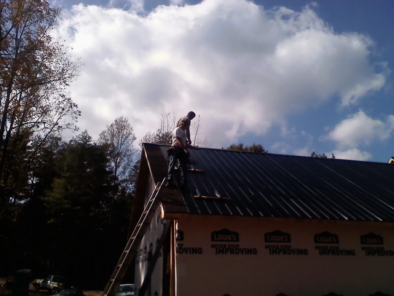 Roofer fastening dark metal panels high against a cloudy sky, from a Roof Inspection job in Shiloh